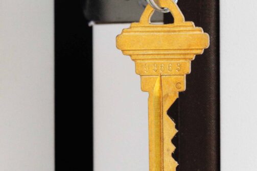 A gold key hanging from a lock on a door.