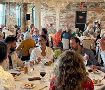 People enjoying a meal together at a cozy, rustic restaurant with brick walls, chatting and laughing around tables.