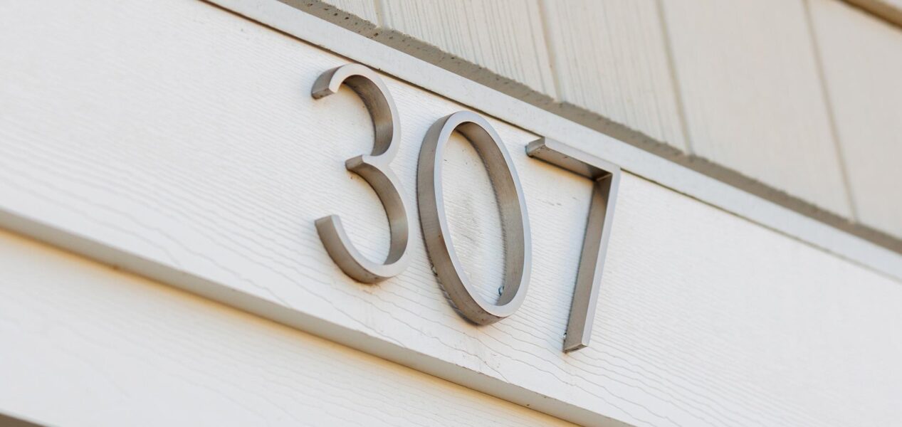 Big metallic numbers showing 307 on the outside wall of a light-colored building.