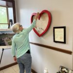 Someone puts something into a big red heart-shaped box on the wall in a cozy room with pictures and certificates.