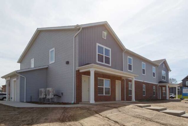 A two-story, modern apartment building with gray siding and brick accents on a sunny day.