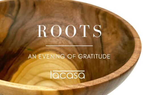 A wooden bowl closeup with the words "ROOTS, An Evening of Gratitude, lacasa" written on it.