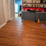 Room with clean wood floors, a broom and mop, a blue cabinet, and shelves filled with various decorations and glassware.